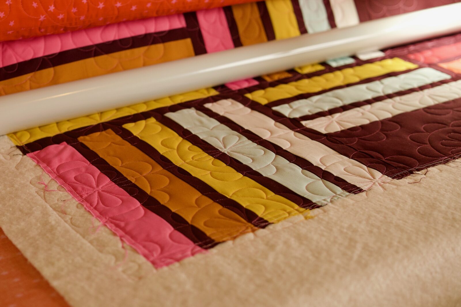 Corner detail of a pink, mustard, and burgundy striped quilt on the frame