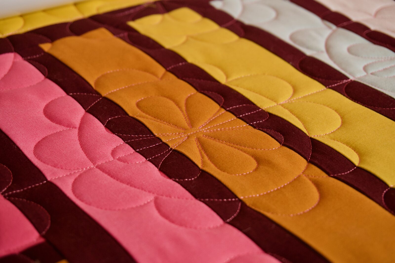 Close up of feather-and-petal quilting pattern on orange and mustard fabric