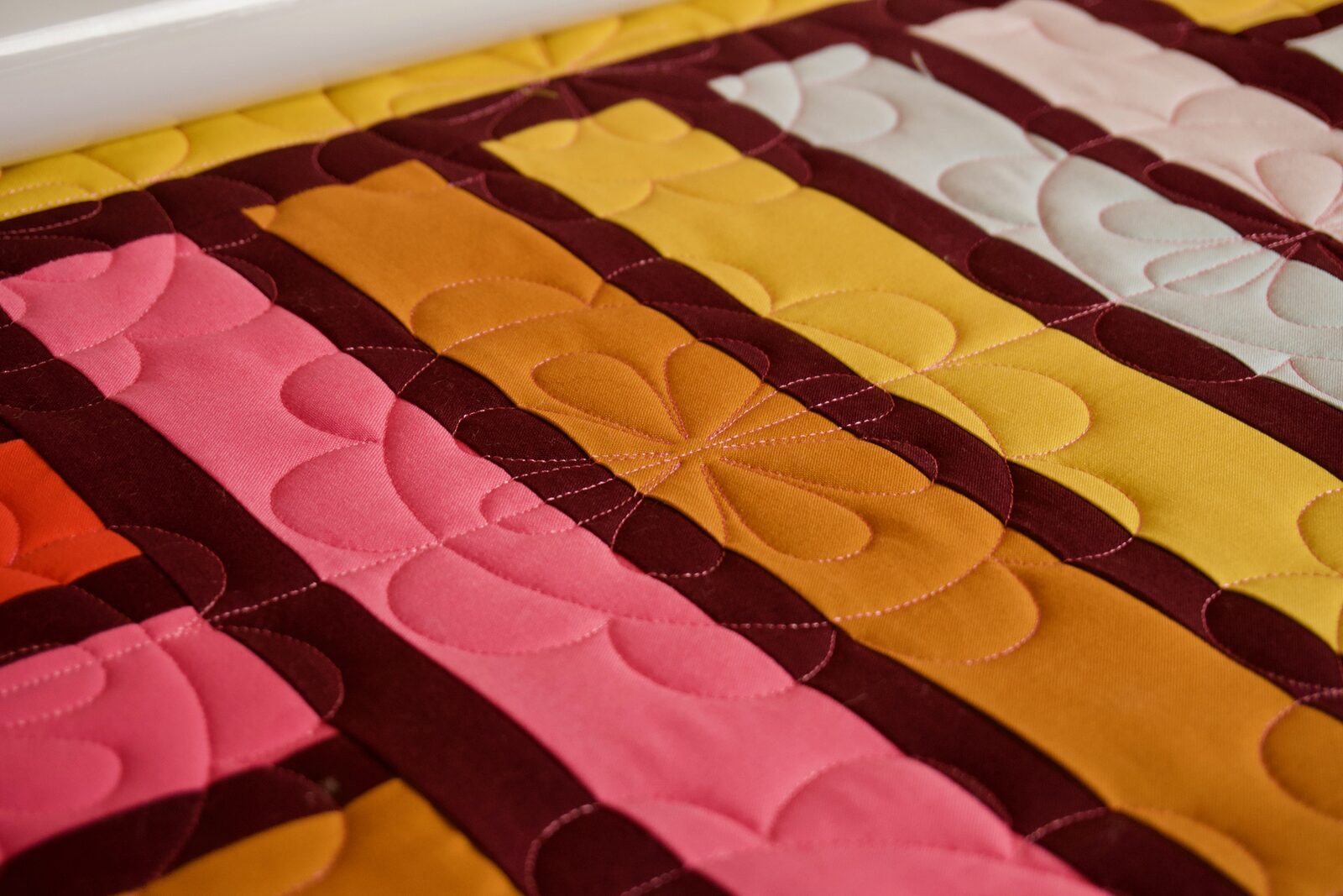 Petal quilting detail on pink, mustard, and cream fabric stripes