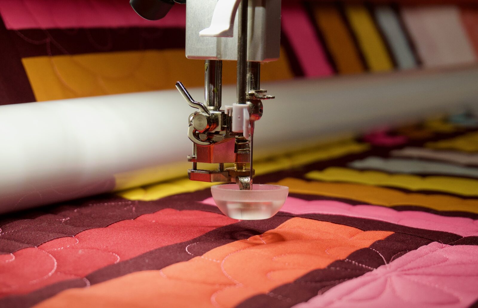 Close up of longarm needle stitching over orange and pink fabric