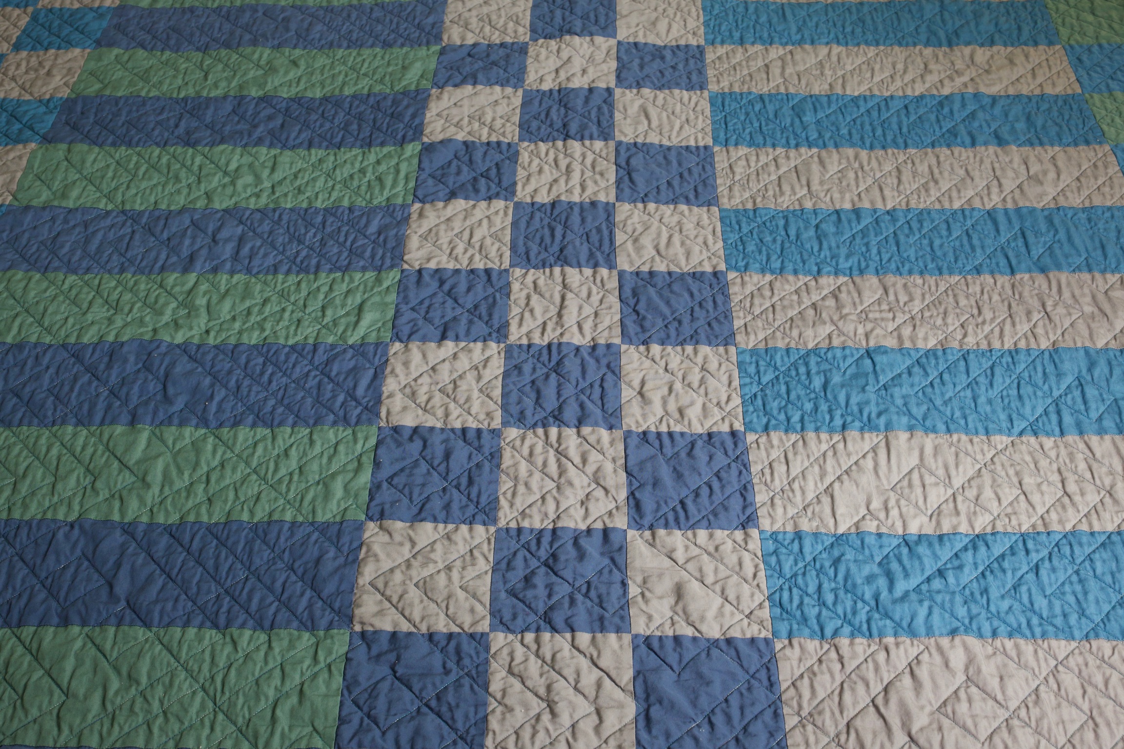 Close-up of navy, gray, and teal patchwork squares with chevron quilting