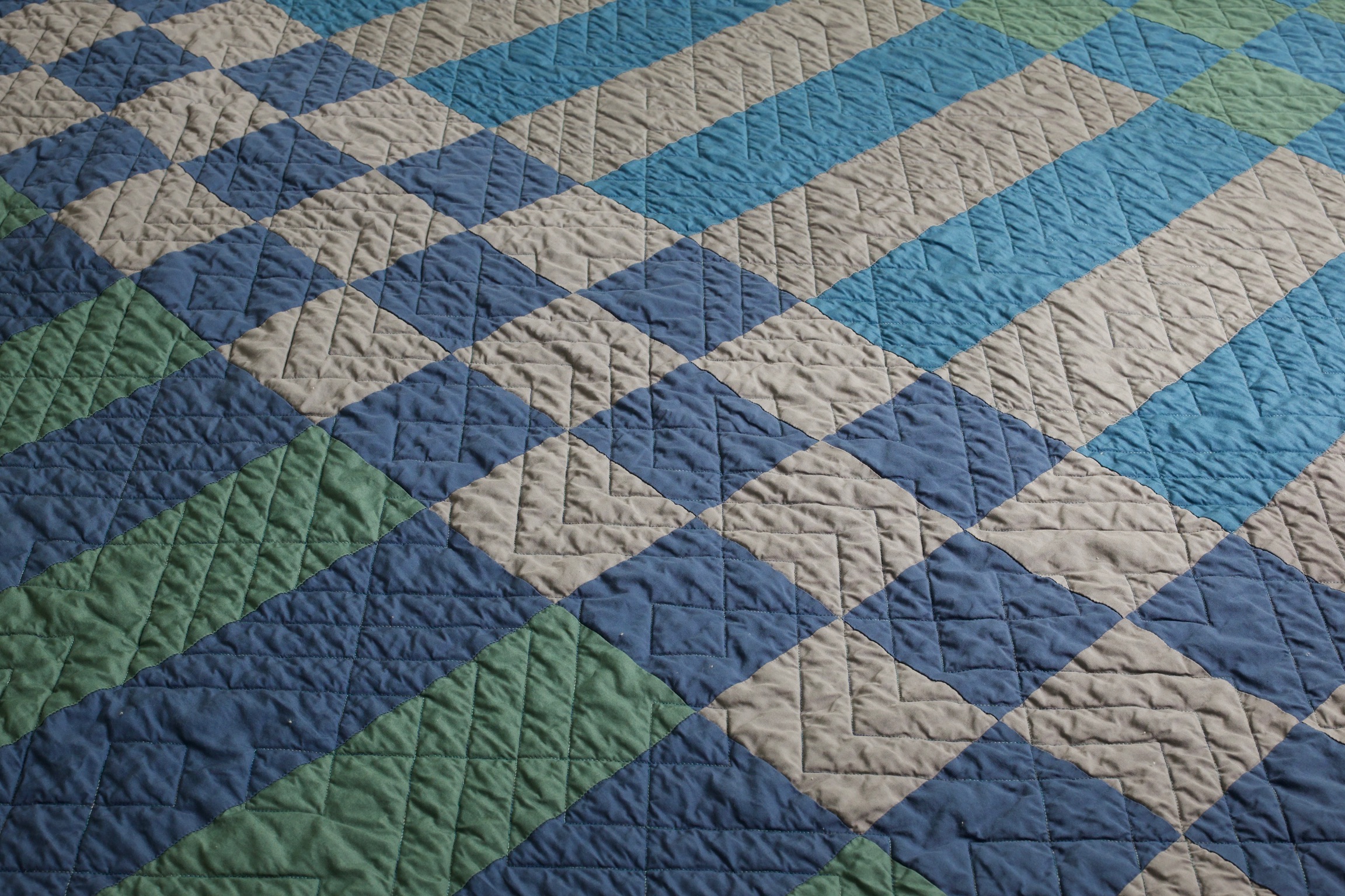 Rectangle patchwork quilt in blue, green, and gray with a diagonal quilting pattern