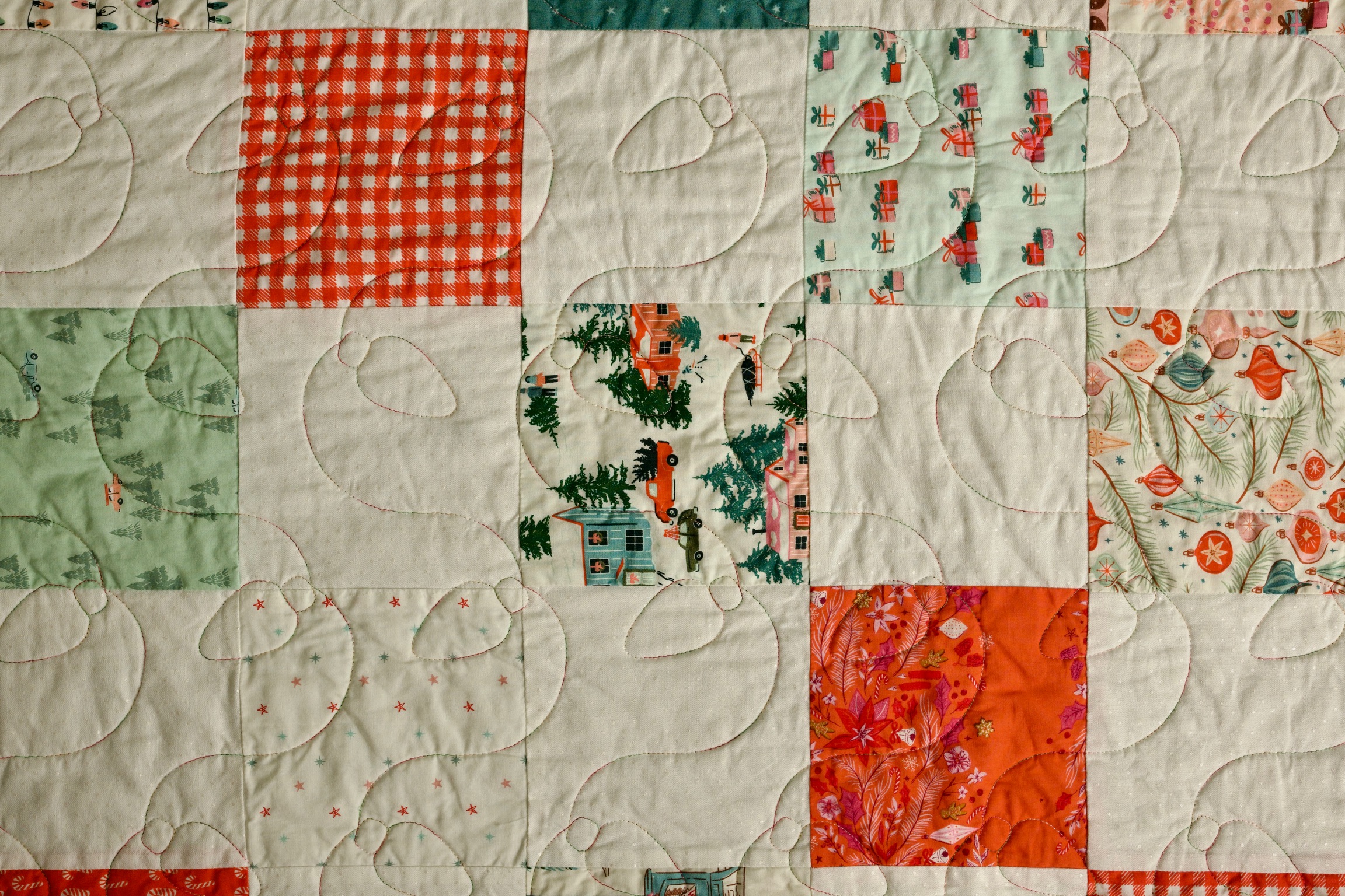 Orange gingham, pine tree, and poinsettia print patchwork squares with loop quilting