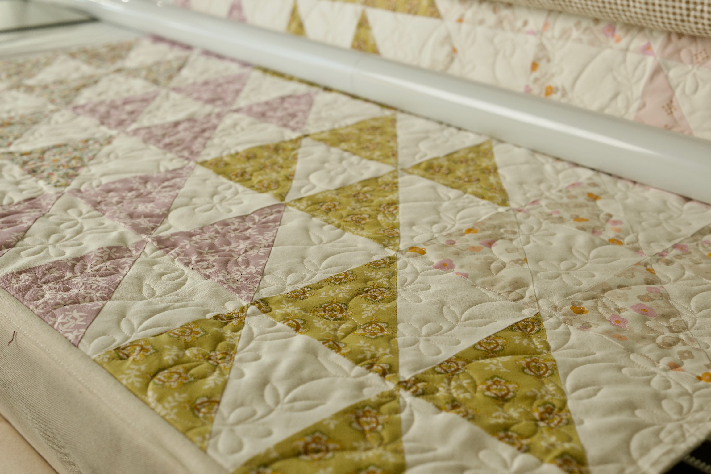 Half-square triangle quilt blocks in blush pink and olive floral prints on the frame