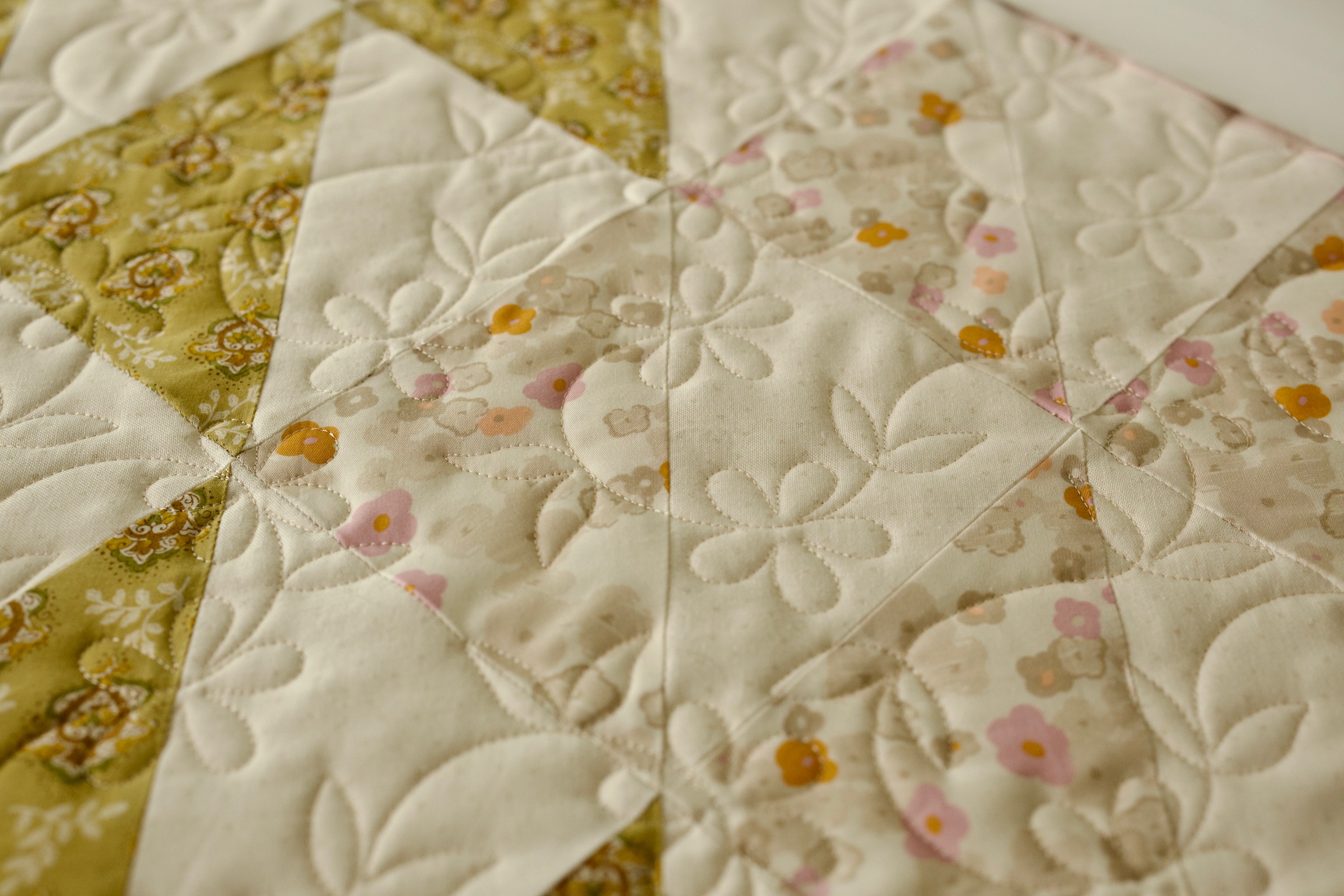 Feather quilting detail over olive and cream floral triangle patchwork