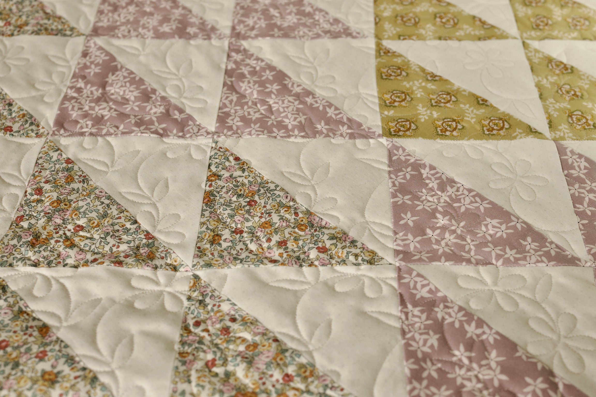 Pinwheel triangle blocks in muted pink and olive florals with feather quilting