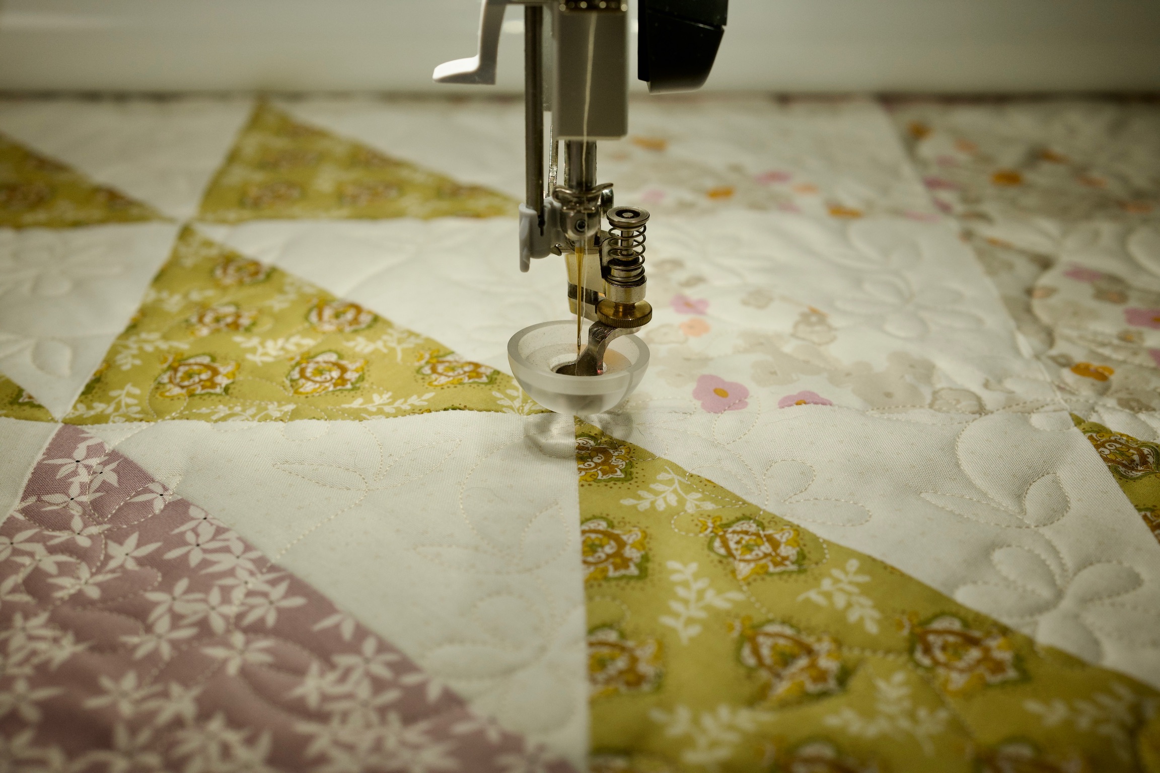 Sewing machine needle stitching feather quilting over the floral triangle quilt