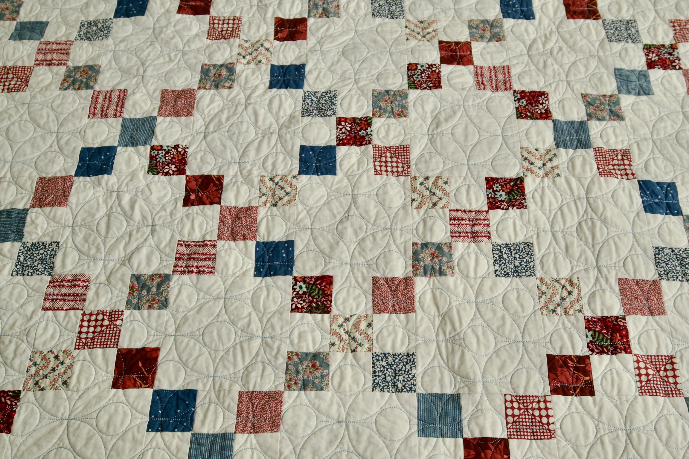 Scrappy patchwork squares in red, cream, and blue florals with allover petal quilting