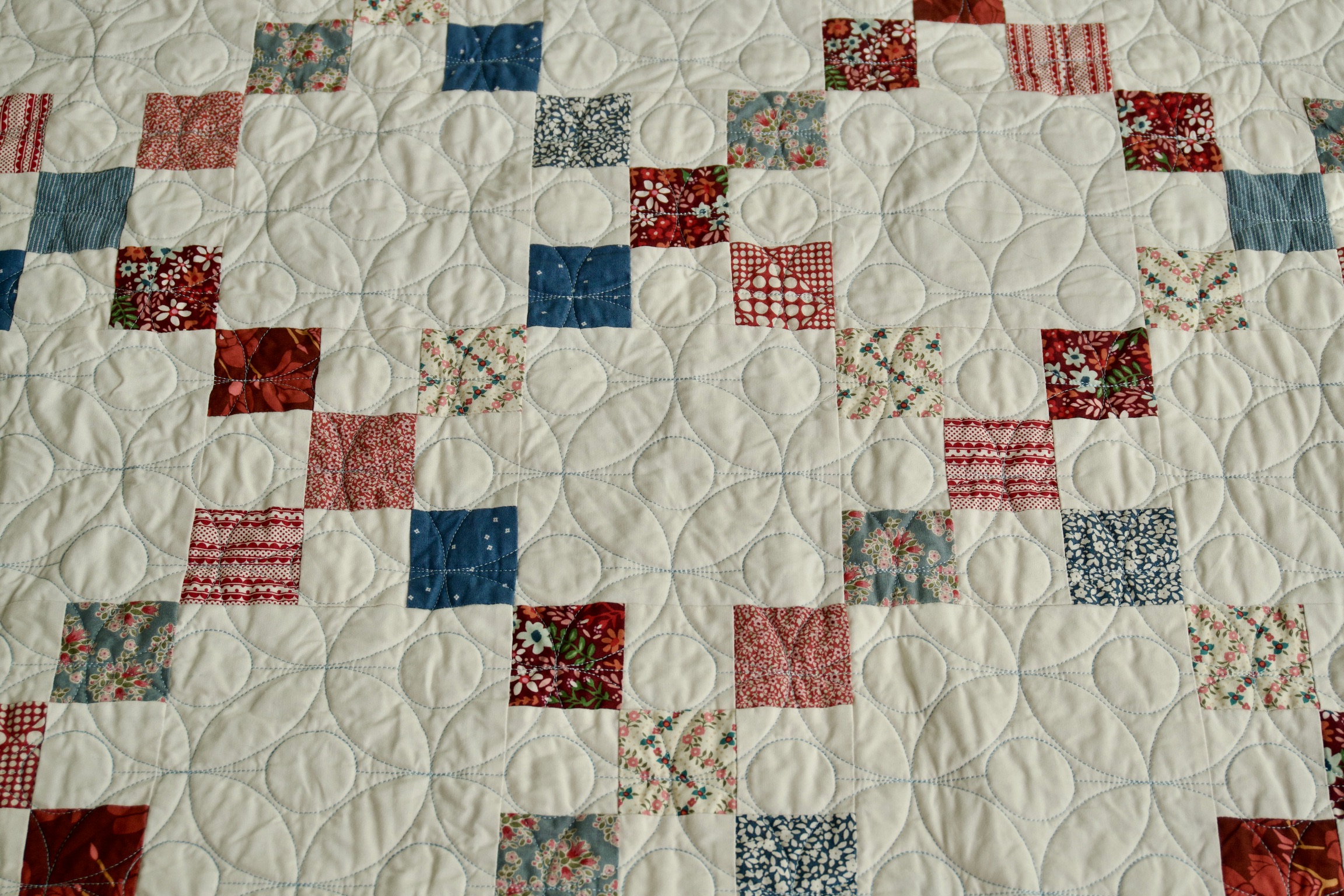 Red, white, and blue scrappy square patchwork with petal quilting stitched throughout