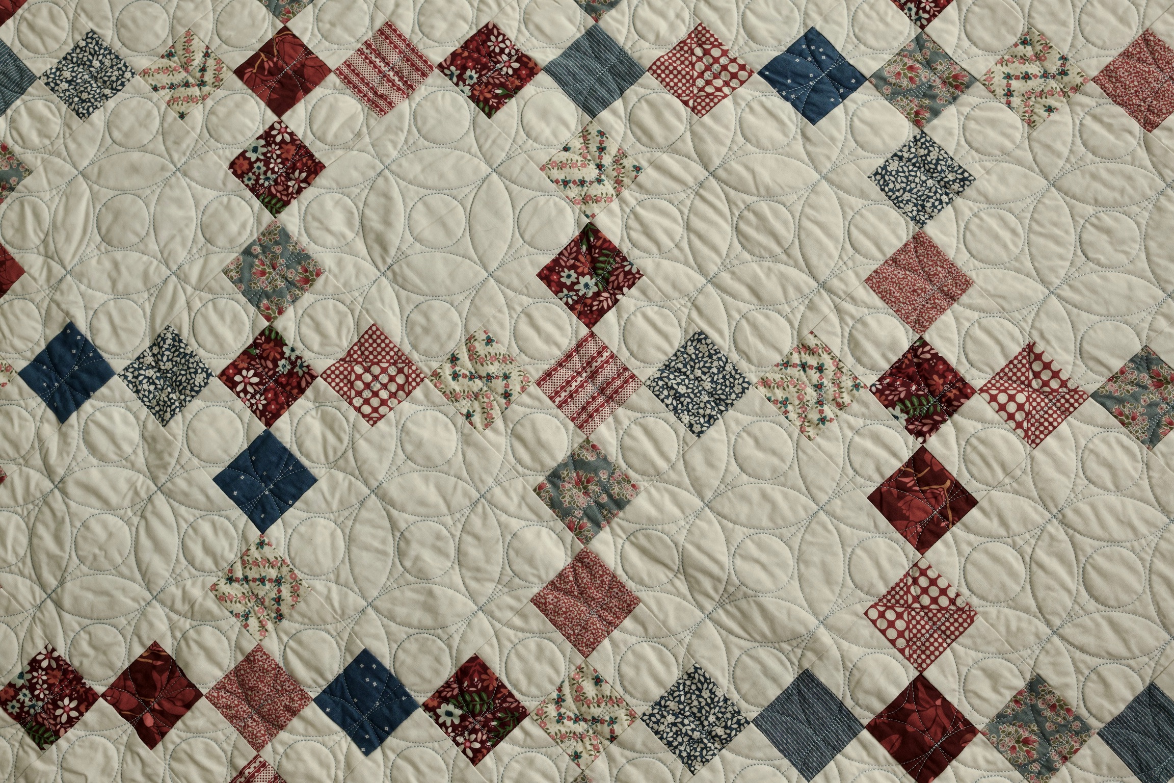 Detail of scrappy red, cream, and blue print squares with petal quilting