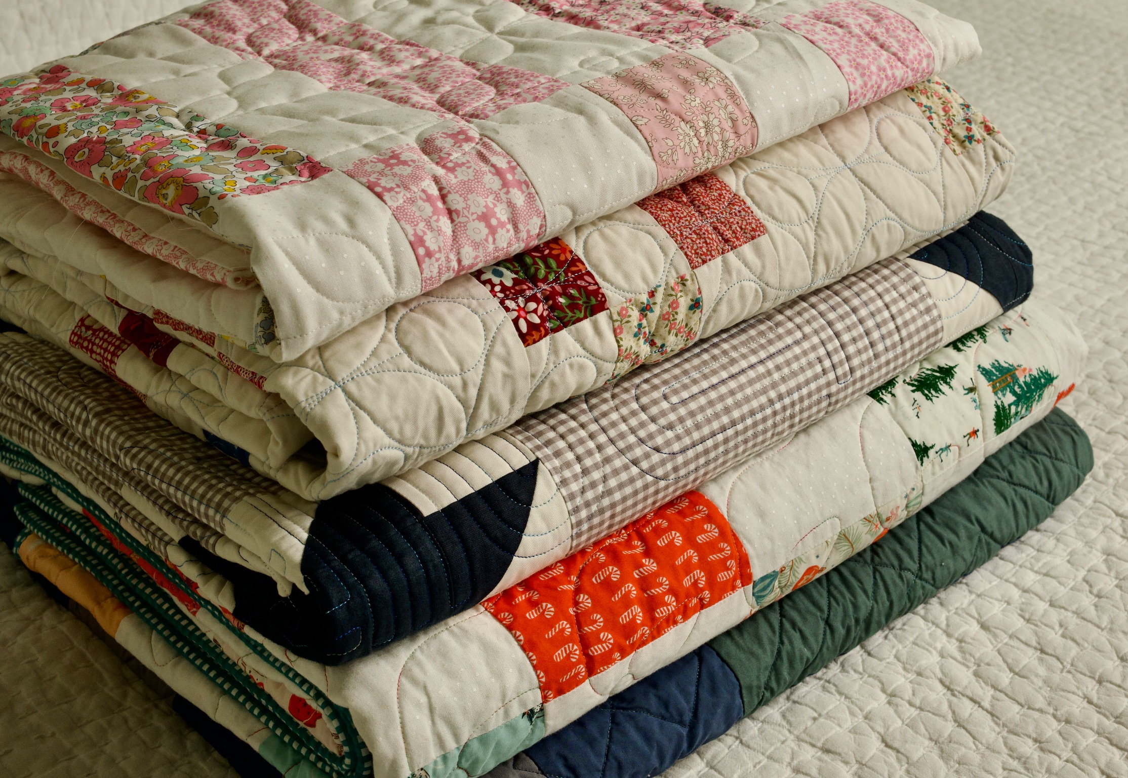 A stack of folded finished quilts in florals, gingham, and holiday prints