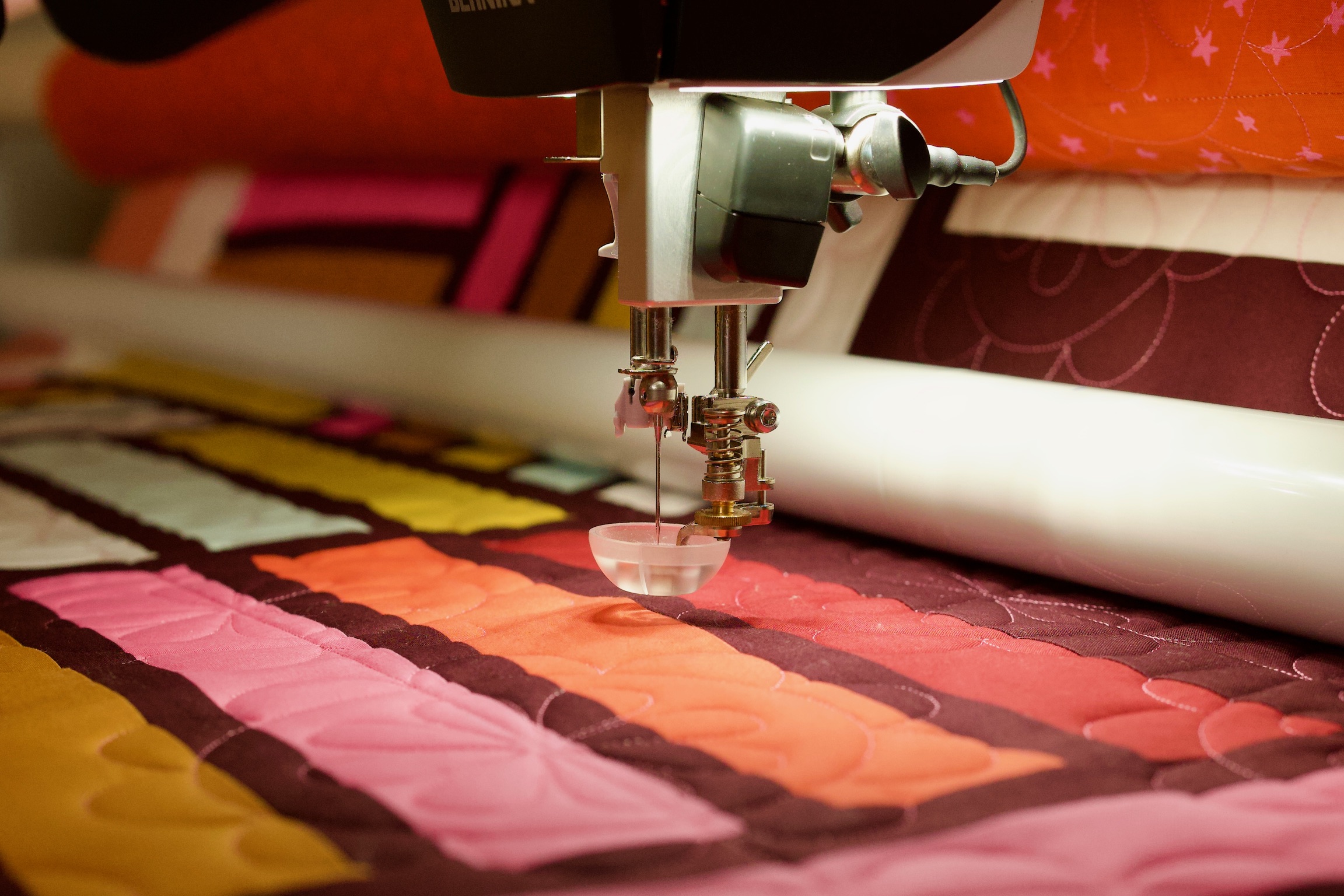 Bernina longarm needle stitching over a pink, orange, and mustard striped quilt